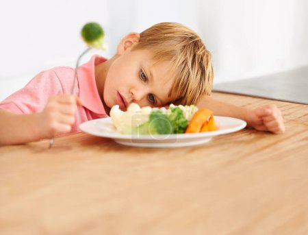 Photo for Sad, hungry and a child with vegetables for dinner, unhappy and problem with food. Frustrated, diet and a little boy eating broccoli and carrots, disappointed with lunch and nutrition for youth. - Royalty Free Image