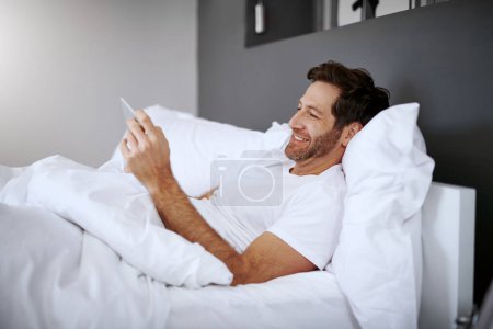 Foto de Este artículo fue una buena lectura. un hombre guapo de mediana edad usando su tableta digital mientras se relaja en su dormitorio - Imagen libre de derechos