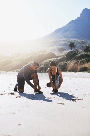 Photo for Lace up and lets get running. a sporty young couple tying their shoelaces while out for a run along the beach - Royalty Free Image