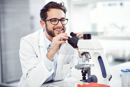 Foto de Hacer del mundo un lugar más feliz. un joven científico alegre mirando a través de un microscopio mientras está sentado dentro de un laboratorio - Imagen libre de derechos