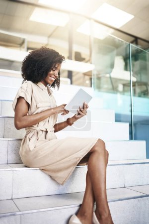Téléchargez les photos : Shell fait ce qu'il faut pour réussir. une jeune femme d'affaires utilisant une tablette numérique assise sur un escalier dans un bureau - en image libre de droit