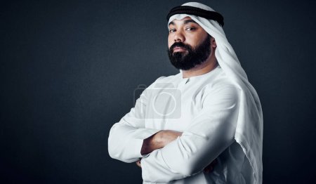 Photo for He believes productivity is the key. Studio shot of a young man dressed in Islamic traditional clothing posing against a dark background - Royalty Free Image