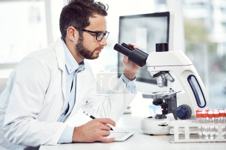 Photo for Some last minute notes. a focused young male scientist making notes and looking through a microscope while being seated inside of a laboratory - Royalty Free Image