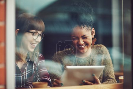 Téléchargez les photos : Ils partagent la meilleure connexion. deux jeunes amis regardant quelque chose sur une tablette numérique dans un café - en image libre de droit