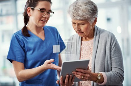 Téléchargez les photos : Vous pouvez voir par vous-même. une jeune infirmière et sa patiente âgée regardant une tablette à la maison de retraite - en image libre de droit