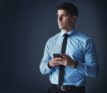 Photo for Send and receive all the updates you need. Studio shot of a young businessman texting on a cellphone against a dark background - Royalty Free Image