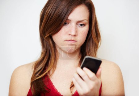 Photo for Phone, text message and an angry woman in studio on a white background unhappy while reading bad news. Social media, internet and app with a young female looking upset while checking her mobile inbox. - Royalty Free Image