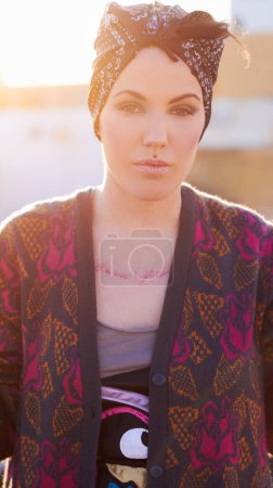 Photo for Portrait, fashion and serious woman in city with scarf on head, urban tattoo and stylish. Face, street and trendy female person from Norway in cool clothes, attitude and body art outdoor at sunset - Royalty Free Image