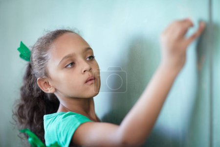 Photo for Education, focus and a girl writing on a chalkboard for learning, studying and teaching in class. Creative, concentration and a young student at a blackboard for a presentation or classroom notes. - Royalty Free Image