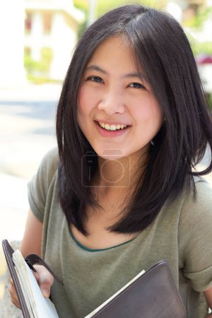 Téléchargez les photos : Portrait, éducation et livre avec une étudiante asiatique sur le campus universitaire pour l'apprentissage ou le développement. Étudier, sourire ou être heureuse avec une jeune étudiante en plein air pour étudier ou apprendre en été. - en image libre de droit