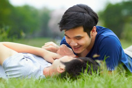 Téléchargez les photos : Hommes asiatiques, couple gay et couché dans le parc, l'herbe ou le jardin avec amour, soin et liaison avec baiser en été. heureux japonais guy romantique et se détendre ensemble sur la pelouse pour lgbtq, sourire, en plein air dans la nature. - en image libre de droit