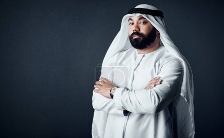 Téléchargez les photos : Je suis là pour affaires. Plan studio d'un jeune homme vêtu de vêtements traditionnels islamiques posant sur un fond sombre - en image libre de droit