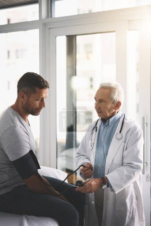 Foto de Tu presión sanguínea está un poco alta. un médico senior que le hace a su paciente masculino un chequeo exhaustivo durante su consulta - Imagen libre de derechos