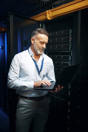 Photo for Lets see if this works now. a mature man using a laptop while working in a server room - Royalty Free Image