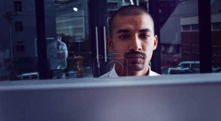 Foto de Así es como se ganó su éxito. un joven hombre de negocios que usa una computadora por la noche en una oficina moderna - Imagen libre de derechos
