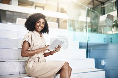Photo for Technology keeps me one step ahead of the game. Portrait of a young businesswoman using a digital tablet while sitting on a staircase in an office - Royalty Free Image