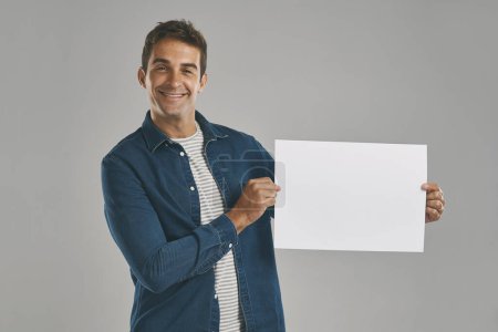 Photo for Id be more than happy to carry your message. Studio portrait of a young man holding a blank placard against a grey background - Royalty Free Image