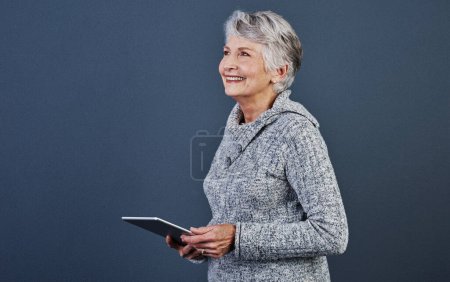 Foto de Ponerse en sintonía con la tecnología de hoy. Estudio de una alegre anciana de pie y usando una tableta - Imagen libre de derechos