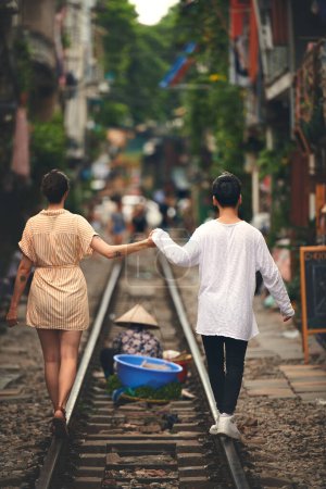 Foto de Cuando encuentres tu alma gemela en la aventura. Vista trasera de una joven pareja caminando en las vías del tren a través de las calles de Vietnam - Imagen libre de derechos