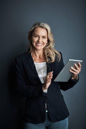 Photo for Who wouldnt choose a simpler way to do business. Studio portrait of a mature businesswoman using a digital tablet against a grey background - Royalty Free Image