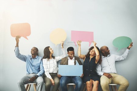 Foto de Diga lo que diga. Captura de estudio de un grupo de empresarios que sostienen coloridas burbujas del habla en línea contra un fondo gris - Imagen libre de derechos