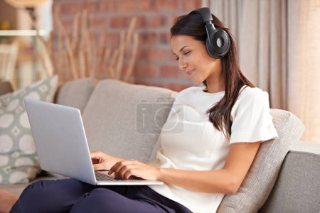 Zuhause, Kopfhörer und eine Frau, die auf einem Laptop tippt und Musik oder Audio hört, während sie online streamt. Glückliche weibliche Person entspannt sich auf dem Sofa, um Radio zu hören oder einen Film mit Internetanschluss anzusehen.