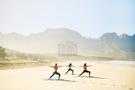 Téléchargez les photos : Sois un guerrier pas un inquiet. trois jeunes femmes pratiquant le yoga sur la plage - en image libre de droit