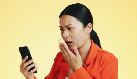 Photo for Asian woman, phone and shocked for bad news, loss or disbelief against a studio background. Female face in shock with facial expression on smartphone for terrible text, message or alert on mockup. - Royalty Free Image