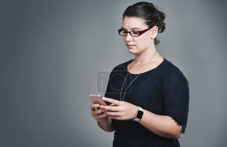 Photo for Interactive business conducted right from her phone. Studio shot of a young businesswoman using a mobile phone against a grey background - Royalty Free Image