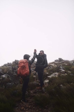 Téléchargez les photos : Le temps a rendu les choses difficiles, mais nous y sommes arrivés. deux amis masculins se donnant un high-five lors de randonnées dans les montagnes - en image libre de droit