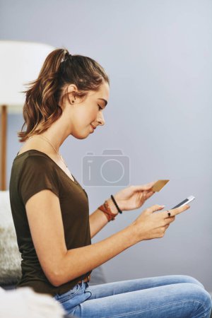 Foto de Encontrarás todo lo que buscas en línea. una hermosa mujer joven usando su teléfono celular y tarjeta de crédito para hacer algunas compras en línea en casa - Imagen libre de derechos