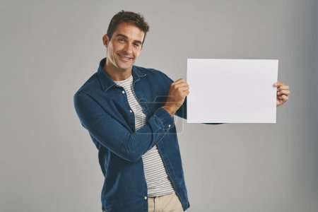 Photo for So what do you think of this. Studio portrait of a young man holding a blank placard against a grey background - Royalty Free Image