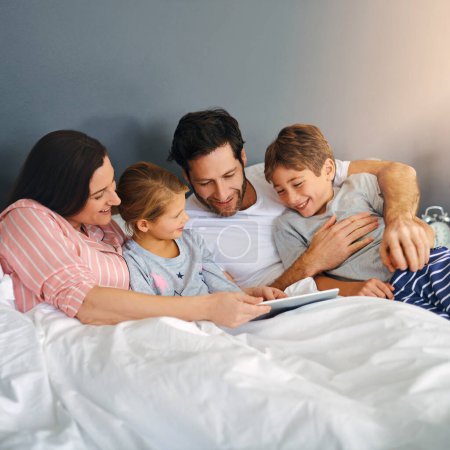 Foto de Pasar tiempo juntos, cualquier oportunidad que tengamos. una familia joven usando una tableta mientras se enfrían en la cama juntos en casa - Imagen libre de derechos
