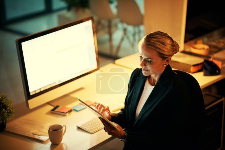 Photo for Theres only one way to prove your dedication. a mature woman using her digital tablet while working late at the office - Royalty Free Image