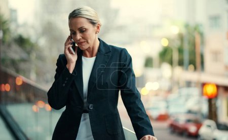 Téléchargez les photos : J'écoute... une jolie femme d'affaires mature qui utilise son téléphone portable tout en se tenant sur le balcon de son bureau - en image libre de droit