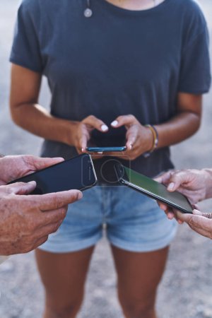 Téléchargez les photos : La famille, notre cercle de soutien. une famille utilisant leurs smartphones ensemble à l'extérieur - en image libre de droit