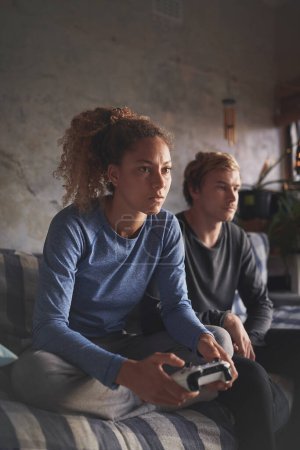 Photo for I dont stop until the game is clocked. a young woman playing computer games while her boyfriend relaxes on the sofa next to her - Royalty Free Image