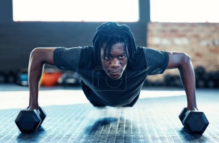 Téléchargez les photos : Il travaille à gagner plus de muscles. un jeune homme faisant des pompes avec des haltères dans une salle de gym - en image libre de droit