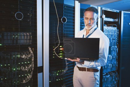 Photo for Keeping things under control and always connected. a mature man using a laptop while working in a server room - Royalty Free Image