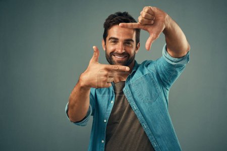 Photo for Frame, hands and face portrait of man in studio on gray background with happiness, confident and smile. Photographer, happy and male person with hand sign for picture, photography and finger border. - Royalty Free Image