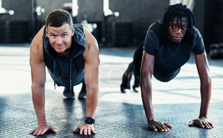 Foto de Las cosas buenas llegan a los que hacen ejercicio. hombres jóvenes haciendo flexiones en un gimnasio - Imagen libre de derechos