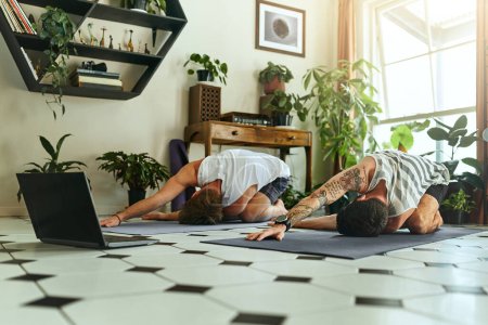 Photo for Wherever theres om, thats your home. two men using a laptop while going through a yoga routine at home - Royalty Free Image