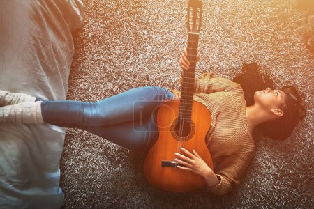 Foto de Terminando el día con una nota musical. una joven relajada tumbada en el suelo y tocando una guitarra acústica en casa - Imagen libre de derechos