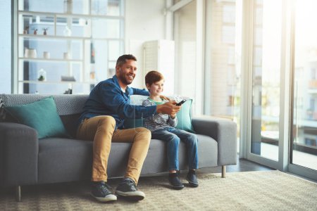 Photo for Switching channels. a cheerful little boy and his father watching television together while being seated on the sofa at home - Royalty Free Image