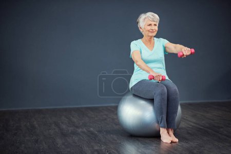 Téléchargez les photos : Elle se consacre à la santé. Plan complet d'une femme âgée travaillant avec des haltères tout en étant assis sur une balle d'exercice - en image libre de droit