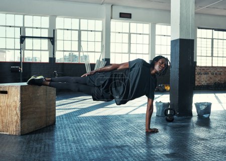 Foto de El tablado es para mente y cuerpo. un joven haciendo una tabla lateral con un bloque de madera en un gimnasio - Imagen libre de derechos