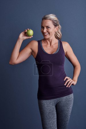 Foto de Mantenga su dieta saludable. Retrato de estudio de una atractiva mujer madura sosteniendo una manzana sobre un fondo azul - Imagen libre de derechos