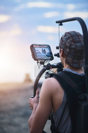 Photo for Look at that view. Over the shoulder shot of a focused young man shooting a scene with a state of the art video camera outside on a beach during the day - Royalty Free Image