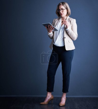 Photo for Using technology in the pursuit of success. Studio shot of an attractive young corporate businesswoman using a tablet against a dark background - Royalty Free Image