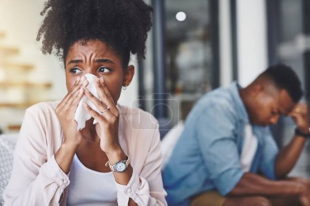 Téléchargez les photos : Comment la grippe a-t-elle pénétré chez nous ? une jeune femme se mouche avec son mari assis à côté d'elle sur le canapé - en image libre de droit